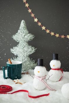 two snowmen are standing in the snow next to a christmas tree and coffee mug