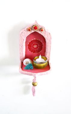 a small pink shelf with a candle and other items in it on a white wall