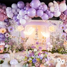 a table topped with lots of balloons and flowers next to a wall filled with animals