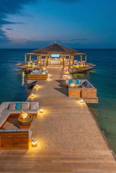 a dock with lounge chairs and lights on it at night time, overlooking the ocean