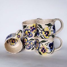 a set of four coffee mugs with painted flowers on them and a saucer