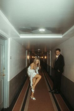 a man standing next to a woman in a white dress on a long hallway between two buildings