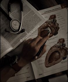 a person's hand holding a pen over an open book with medical diagrams on it