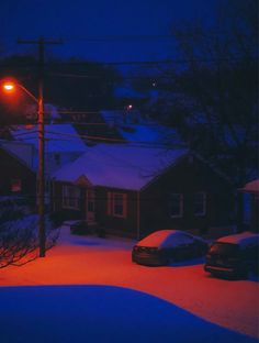 cars are parked in the snow at night with street lights shining on houses and trees