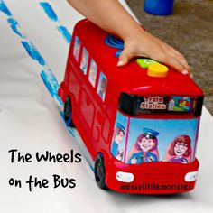 a child's hand on top of a toy bus with the wheels on the bus