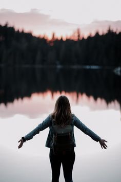 a woman standing in front of a body of water with her arms spread wide open