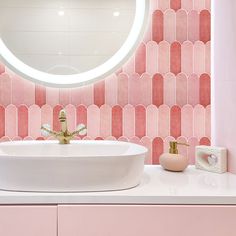 a white sink sitting under a round mirror next to a pink counter top with gold faucet