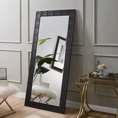 a large mirror sitting on top of a wooden floor next to a chair and table