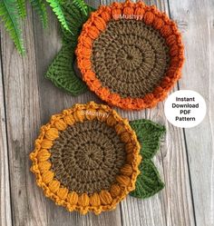 two crocheted sunflowers sitting on top of a wooden table next to a fern