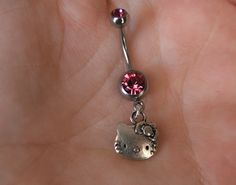 a person is holding onto a tiny belly ring with a hello kitty charm on it