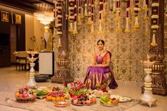 a woman sitting on the floor surrounded by fruits and vegetables in front of a decorated stage