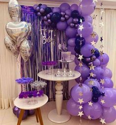 purple and silver balloons are hanging from the ceiling next to a table with cake on it