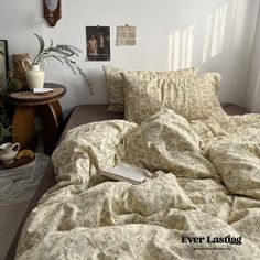 an unmade bed in a bedroom next to a table with a potted plant on it