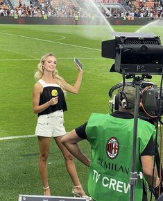 a female soccer player is spraying water on the field with her camera and another person