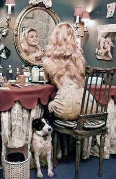 a woman sitting at a table in front of a mirror with a dog standing next to her