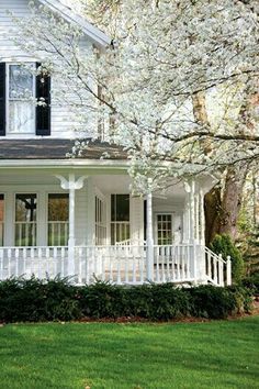 a white house with black shutters on the front porch and trees in blooming