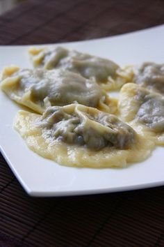 three ravioli with gravy on a white plate sitting on a brown table