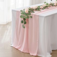 the table is decorated with pink flowers and greenery on it, along with white linens