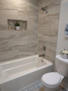 a white toilet sitting next to a bath tub in a bathroom with gray tile on the walls