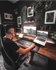 a man sitting at a desk with two laptops and a desktop computer on it