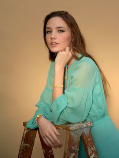 a young woman sitting on top of a wooden chair next to a ladder with her hand under her chin