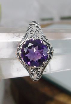 Natural Amethyst Ring Daisy Design#66 In Stock Size 6 Inspired by the Art Nouveau movement of the early 20th century, I now offer this lovely reproduction filigree ring in sterling silver. This gorgeous ring is set with a genuine/natural 1.5ct purple amethyst gemstone; which has a great shine and very good clarity. The round full cut purple amethyst gemstone is 8mm (5/16th of an inch) in diameter. The ring measures 12mm NS on the finger. The inside of the band is marked 925 for sterling. Notice Purple Amethyst Ring With Intricate Design For Promise, Purple Amethyst Promise Ring With Intricate Design, Purple Amethyst Ring With Intricate Design, Filigree Amethyst Ring For Anniversary, Amethyst Ring With Intricate Design, Ornate Round Purple Amethyst Ring, Ornate Purple Amethyst Ring, Amethyst Filigree Ring, Intricate Design Purple Amethyst Ring