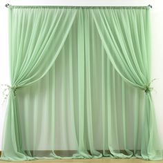 a green curtain hanging on the side of a white wall next to a wooden floor