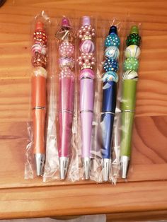 four different colored pens sitting on top of a wooden table next to some beads and pearls