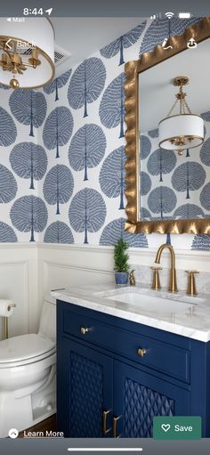 a blue and white bathroom with gold accents on the mirror above the sink is an ornately designed wallpaper