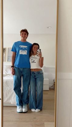 a man and woman standing in front of a mirror taking a selfie with their cell phone