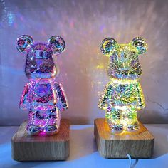 two lighted teddy bears are sitting on wooden bases, one is multicolored and the other is white