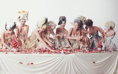 a group of women sitting on top of a white table covered in flowers and petals