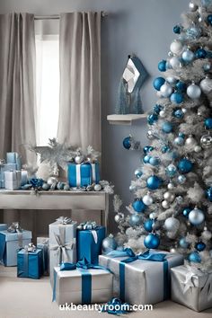 a christmas tree with blue and silver presents under it in front of a window filled with curtains