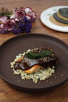 a brown plate topped with meat and rice on top of a wooden table next to flowers