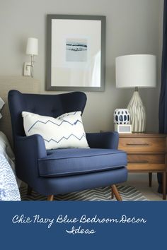 a blue chair sitting in front of a lamp next to a dresser with a painting on it