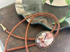 This awesome bolo tie has a southwestern design and genuine crazy lace agate centerpiece stone (it has cream/red/orange/burgundy tones). Each stone is different, it won't be exactly the one pictured but will be similar. The cord is genuine brown leather with matching brass metal tips. Our bolos pair nicely with many of our belt buckles! They make wonderful gifts. The western bolo tie rope length is 39'' ; pendant size is 1 1/2'' x 1 1/4'' Stone itself is 30mm x 40mm Southwestern Style Jewelry With Sliding Knot For Gifts, Southwestern Jewelry With Sliding Knot As A Gift, Bohemian Lariat Bolo Ties As Gift, Bohemian Brown Bolo Tie As Gift, Artisan Bolo Tie With Sliding Knot As Gift, Artisan Bolo Ties With Sliding Knot For Gift, Southwestern Style Jewelry As A Gift, Southwestern Style Jewelry As A Gift With Adjustable Length, Western Style Jewelry With Adjustable Cord For Gift