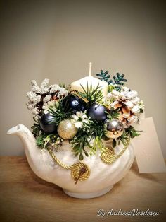 a white teapot filled with ornaments and greenery on top of a wooden table