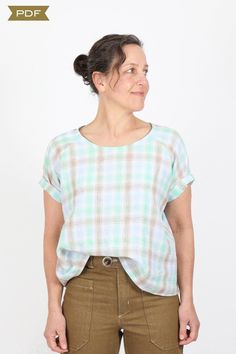 a woman standing in front of a white wall wearing brown pants and a plaid shirt