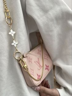 a woman holding onto a pink purse with gold chains on her neck and white shirt behind her