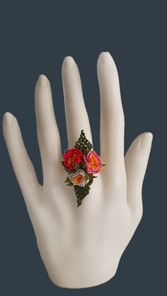 a hand with a ring on it that has flowers in the middle and two leaves at the bottom