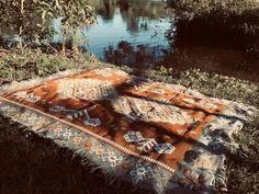 an orange and white rug sitting on the grass next to a body of water with trees in the background