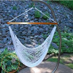 a white hammock hanging from a metal stand in front of some rocks and plants