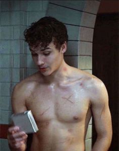 a shirtless young man is looking at his book