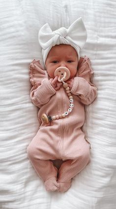 a baby is laying down with a pacifier in it's mouth and wearing a pink outfit