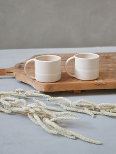 two white cups sitting on top of a wooden tray