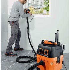 a man is using a vacuum to clean the floor in front of a window with an orange and black blow dryer