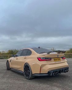 the rear end of a tan bmw car parked in a parking lot on a cloudy day