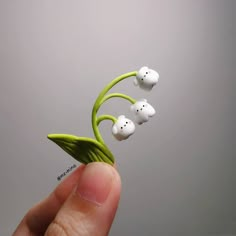 a hand holding a tiny toy with three white heads on it's tip and two green stems in the middle