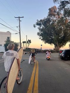 two people riding bikes with surfboards on their backs and one person holding a surfboard