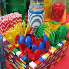 there are many legos in the box on the table with plates, cups and candy